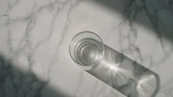 gnistrande vatten i en klar glas med solljus gjutning dynamisk skuggor på en marmor yta, skapande en uppfriskande, lysande, och minimalistisk dryck scen full av naturlig klarhet och visuell textur video