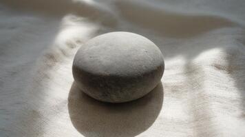 lugn slät grå sten vilar på mjuk texturerad beige tyg med mild brokig solljus skapande en fredlig harmonisk atmosfär av naturlig lugna video