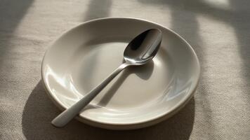 luz solar jogando através uma minimalista mesa configuração com uma imaculado prato e brilhando colher criando uma limpar \ limpo brilhante atmosfera do antecipação para uma delicioso refeição adiante video