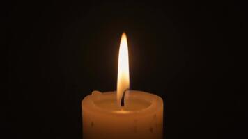 Soft glowing candle flame gently flickering in the quiet darkness creating a serene and calming atmosphere that symbolizes hope warmth and light within a deep shadowed backdrop video