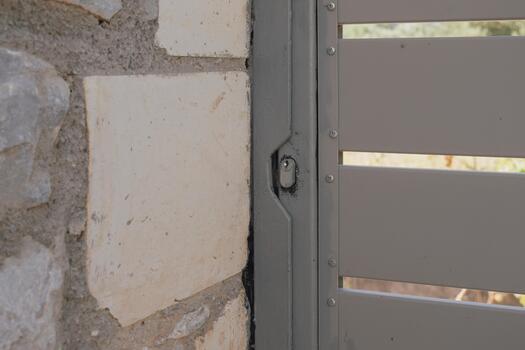 Close-up of a shabby poorly painted modern gate lock cylinder embedded in a metal frame next to a stone wall. Focus on the flawed deteriorating surface and textured materials photo