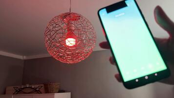 kvinna hand aktiverande färgskiftande läge på smart kristallkrona genom mobil app som rum fyllningar med flerfärgad lampor video