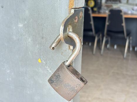 Close-Up of a Rusty Padlock on a Metal Door with Blurred Background showing Chairs and Table photo