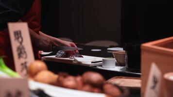 vicino su Spettacoli mani affettare rosso pesce su un' bianca tavola nel tokyo. caldo Basso chiave illuminazione, superficiale profondità di campo, forte bokeh, pulito sashimi righe, ritmico movimento. video