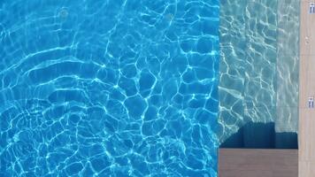 aereo superiore giù Visualizza di un' rettangolare piscina con in profondità blu bacino sinistra, piastrelle passaggi e legna ponte Giusto, pavimento scarichi e 0,60 m marcatori visibile, luminosa mezzogiorno leggero video