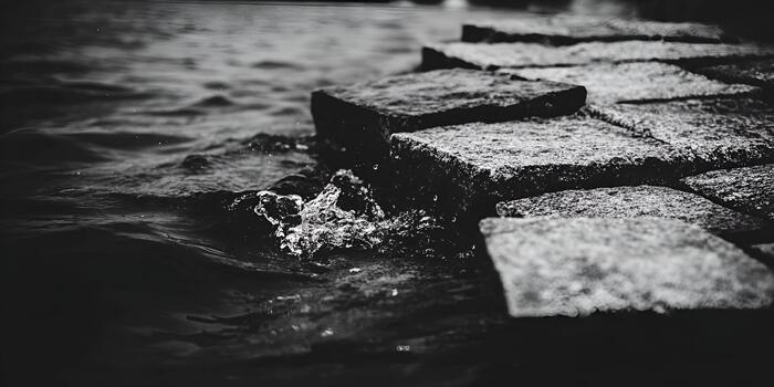 Grayscale water ripples and splashes gently against old stone blocks creating a moody natural scene photo
