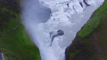 High angle aerial view of Gullfoss on the Hvita river in the Golden Circle as white water cascades into a steep canyon, with mist, rainbows, and busy viewing paths. video