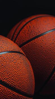 Two Basketballs Illuminated in Warm Light on a Dark Background During a Nighttime Sports Event. photo