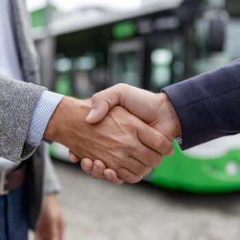 Two businessmen shake hands in front of a green public transport bus, symbolizing partnership and collaboration. photo