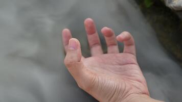 delicato mano raggiungendo su in direzione fluente acqua nel un' sereno naturale ambiente cattura la tranquillità e connessione con nature elemento video