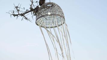Unique handmade decorative lantern hanging from a tree branch against a serene sky backdrop, showcasing intricate design and natural elements in harmony video