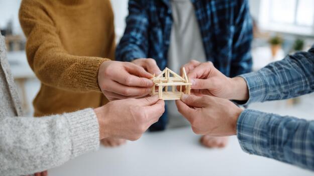 A diverse group of adults collaboratively holding a small wooden house model, symbolizing teamwork and creativity in construction. photo