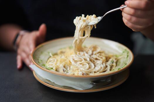 Appetizing carbonara paste with chicken improperly wound on fork. Spaghetti inaccurately hanging and falling from fork. Close up photo