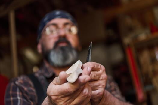 Man carving wood with a knife in workshop, craftsperson creating wooden figure, hobby and woodworking concept, artisan at work, handmade project, skill and creativity. photo