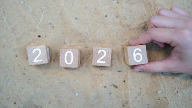 Hand Placing Wooden Blocks Showing Number 2026 on Sandy Background for Concept of Future Year and Progress in Time Management and Planning photo