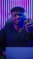 afrikansk amerikan man i hörlurar med bärbar dator som visar tumme upp i mörk neon trogen Plats i stol nöjd futurism kille manlig kodare gamer programmerare hacker rekommendera dator modern cyberrymden video