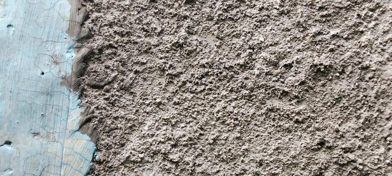 Rough cement walls with a sandy, uneven surface and traces of peeling blue paint along the edges. photo