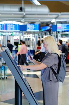 Traveler using a self-service kiosk at the airport to check in for a flight while others move through the busy terminal photo