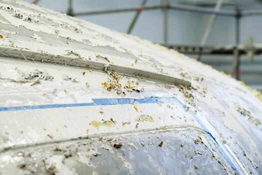 Work in progress on a boat hull covered in paint and debris inside a workshop with scaffolding capturing the scene of boat restoration during daylight hours photo