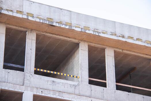 Concrete Wall Frame of Building under Construction. Formwork Prints Surface with Thermal Pads, black-yellow Fence. Monolithic box with window holes Construction Site. Architectural origin Structure. photo