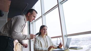 ufficio colleghi collaboratore a opera. compagni di squadra Guarda a il computer portatile e discutere attività commerciale questioni. Basso angolo Visualizza. panoramico finestre a sfondo. video