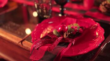 Festive red plate with wavy edges and Christmas decoration on top. Artificial greenery and berries tied up with sparkling red ribbon. Blurred backdrop. video
