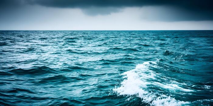 Dynamic deep blue ocean waves with white foam crest under a moody overcast sky photo