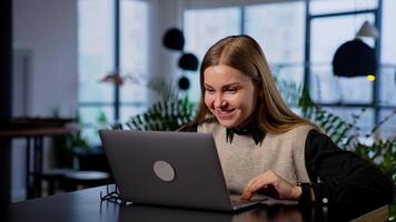 elástico sonriente joven mujer trabajando en su computadora. contento dama es satisfecho con algunos resultado y hace un éxito gesto. borroso fondo. video