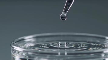 en klar flytande släppa delikat falls från en exakt pipett, alstrande fascinerande koncentrisk krusningar tvärs över de ren vatten yta i en rena, vetenskaplig laboratorium miljö video