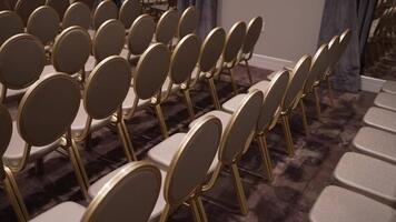 rader av tömma, elegant guld stolar anordnad på en mönstrad matta för en formell händelse. de scen föreslår förväntan för en bröllop, konferens, eller ceremoni. idealisk för händelse planera begrepp. video