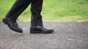 detailopname van een man's poten in zwart jurk broek en schoenen wandelen Aan een pad. de tafereel overbrengt een zin van doel en formaliteit. gebruik voor bedrijf, reis, of evenement concepten. video