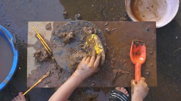 en barn crafting med lera, använder sig av en skyffel och ätpinnar till skapa en unik bit av konst. de barnets händer är upptagen på arbete, och de verktyg är ordentligt placerad på de trä- yta. video
