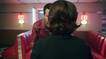 en handhållen kamera snurrar runt om två tecken i en diner under en uppvärmd argument. neon ljus blinkar röd och vit som de kamera nedskärningar skarpt mellan dem. filmiska live-action, mättad Färg grad video