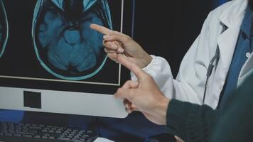 A doctor pointing at a computer screen with a brain scan video