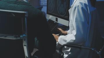 A doctor is working on a computer while another person looks at it video