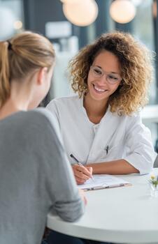 Smiling doctor writing notes during consultation with patient photo