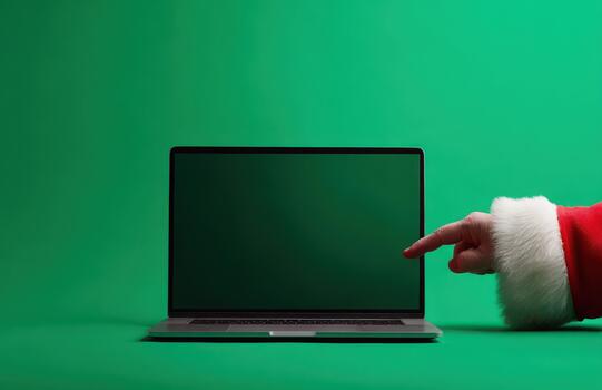 Santa pointing at blank laptop screen on green background photo