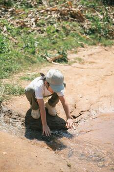 Child Exploring Nature by Stream Water, Touching Water Surface with Hands, Curiosity and Discovery in Natural Environment, Playful Outdoor Experience photo