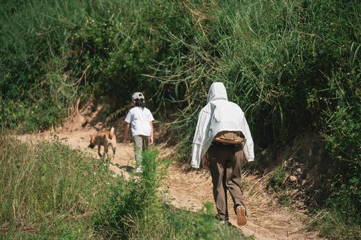 Two Individuals Walking on a Trail Surrounded by Greenery with a Dog, Capturing a Moment of Outdoor Exploration and Connection with Nature photo