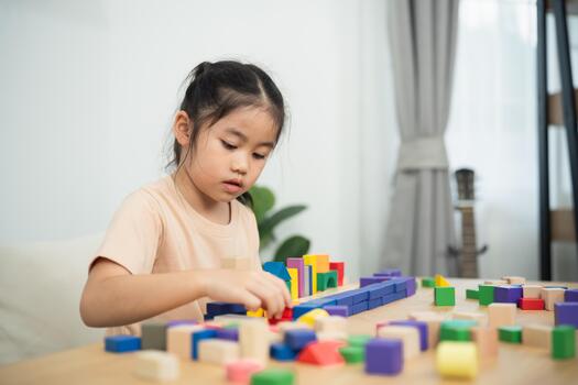 Young girl engaged in creative building play with colorful wooden blocks on a table in a bright, modern learning environment at home photo