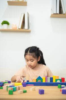 Young Girl Engaged in Creative Play with Colorful Building Blocks on a Wooden Table in a Bright Indoor Setting photo