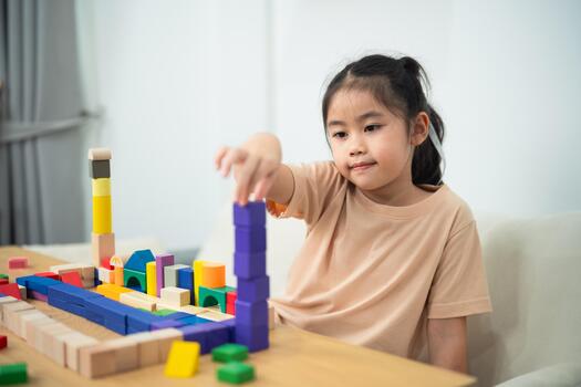 Young Girl Stacking Colorful Building Blocks in Bright Room, Engaged in Educational Playtime Activity, Developing Creativity and Motor Skills photo