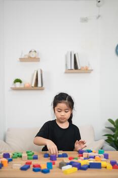 Focused girl building with colorful blocks on wooden table in modern living room, engaging in creative play, enhancing motor skills and cognitive development photo