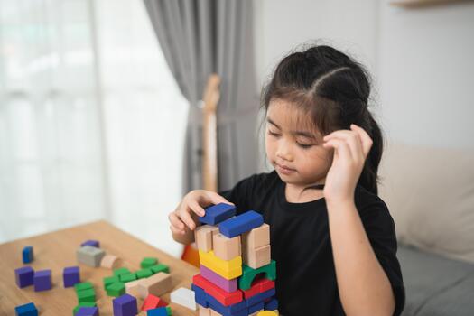 Young Child Engaged in Creative Play with Colorful Building Blocks in Cozy Indoor Space, Focused on Constructing Tower of Various Shapes photo