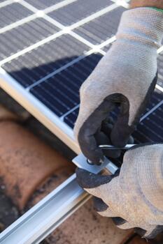 Man technician in work gloves installing stand-alone photovoltaic solar panel system under beautiful blue sky with clouds. Concept of alternative energy and power sustainable photo