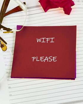 A red card stating WIFI PLEASE sits atop a lined notebook, near glasses and a red tissue. It looks like someone needs to connect to the internet photo