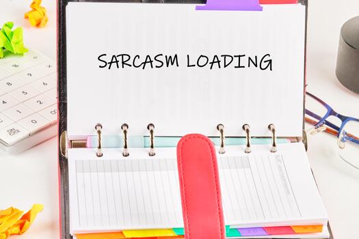 A day planner is open, displaying the words Sarcasm Loading. Next to it are a calculator, crumpled paper, and glasses, suggesting a busy workspace and a humorous approach to the day photo