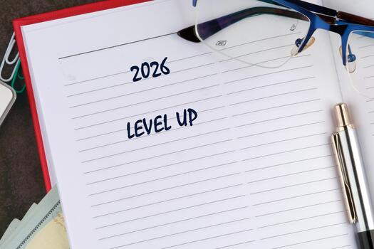 An open notebook on a desk shows the date 2026 and the phrase Level UP written on a lined page, accompanied by glasses and a pen suggesting plans and preparation photo