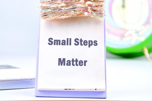 A desk calendar sits open, displaying the motivational message Small Steps Matter, while nearby, a calculator and a clock suggest a focus on time and progress photo