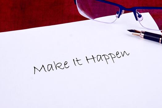 A motivational statement encouraging action is handwritten on a clean sheet of paper. Reflections from reading glasses and a fountain pen add a touch of creativity to the workspace photo